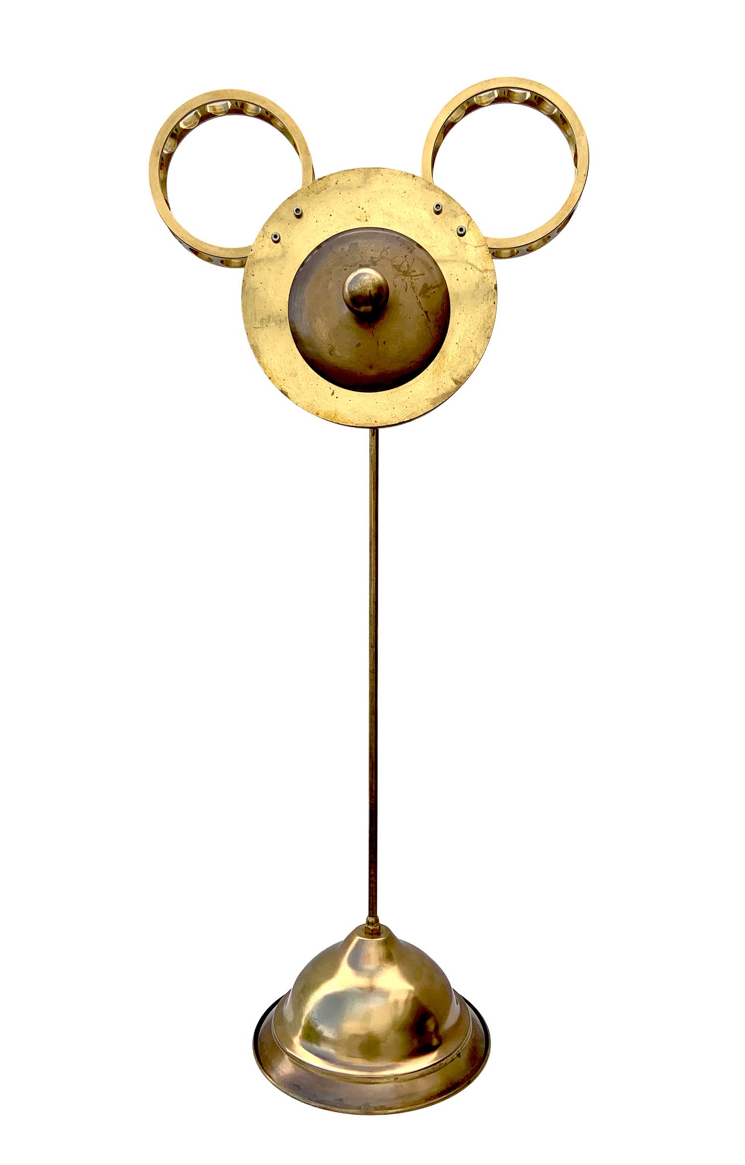 Una escultura con un rostro formado por una esfera con un pomillo a modo de nariz y soportes industriales a modo de orejas; cuenta con una base de la que surge un tallo que sostiene la cabeza.