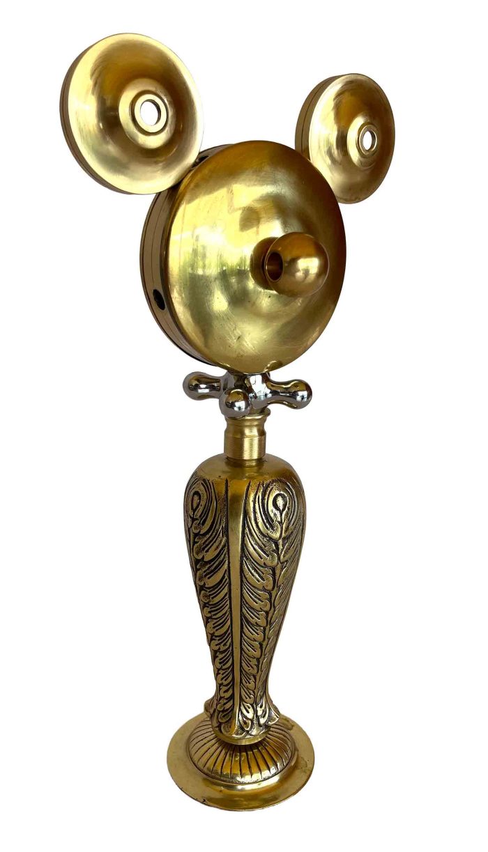 Una escultura dorada con el cuerpo y las piernas decorados con motivos ornamentados, y una pieza con forma de maneta que hace las veces de collar.