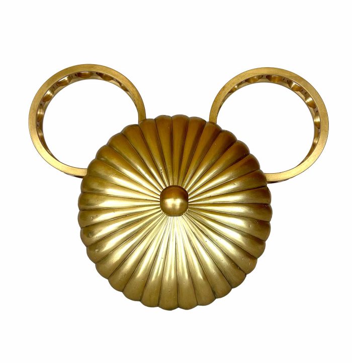 Una escultura con la cara de Mickey para colgar en la pared, hecha con una pantalla de lámpara con rayas radiales como las del sol y dos círculos industriales a modo de orejas.