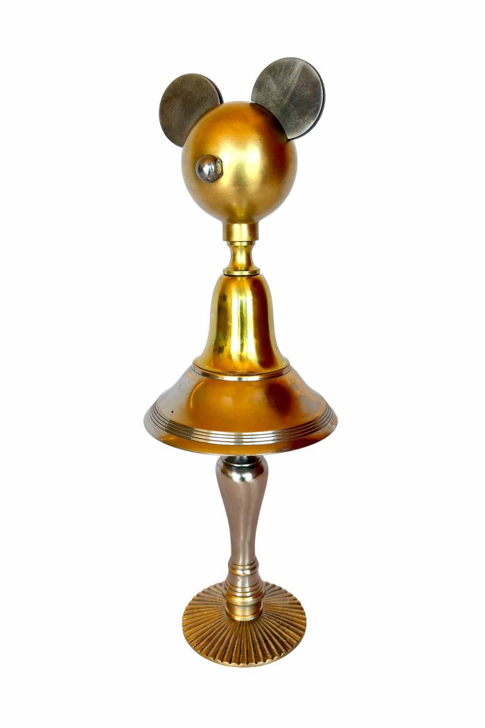 Una escultura dorada compuesta por un pomo a modo de rostro, piezas marinas de Cosir a modo de orejas, un cuerpo y un molde con partes de lámpara, y las patas de un candelabro.