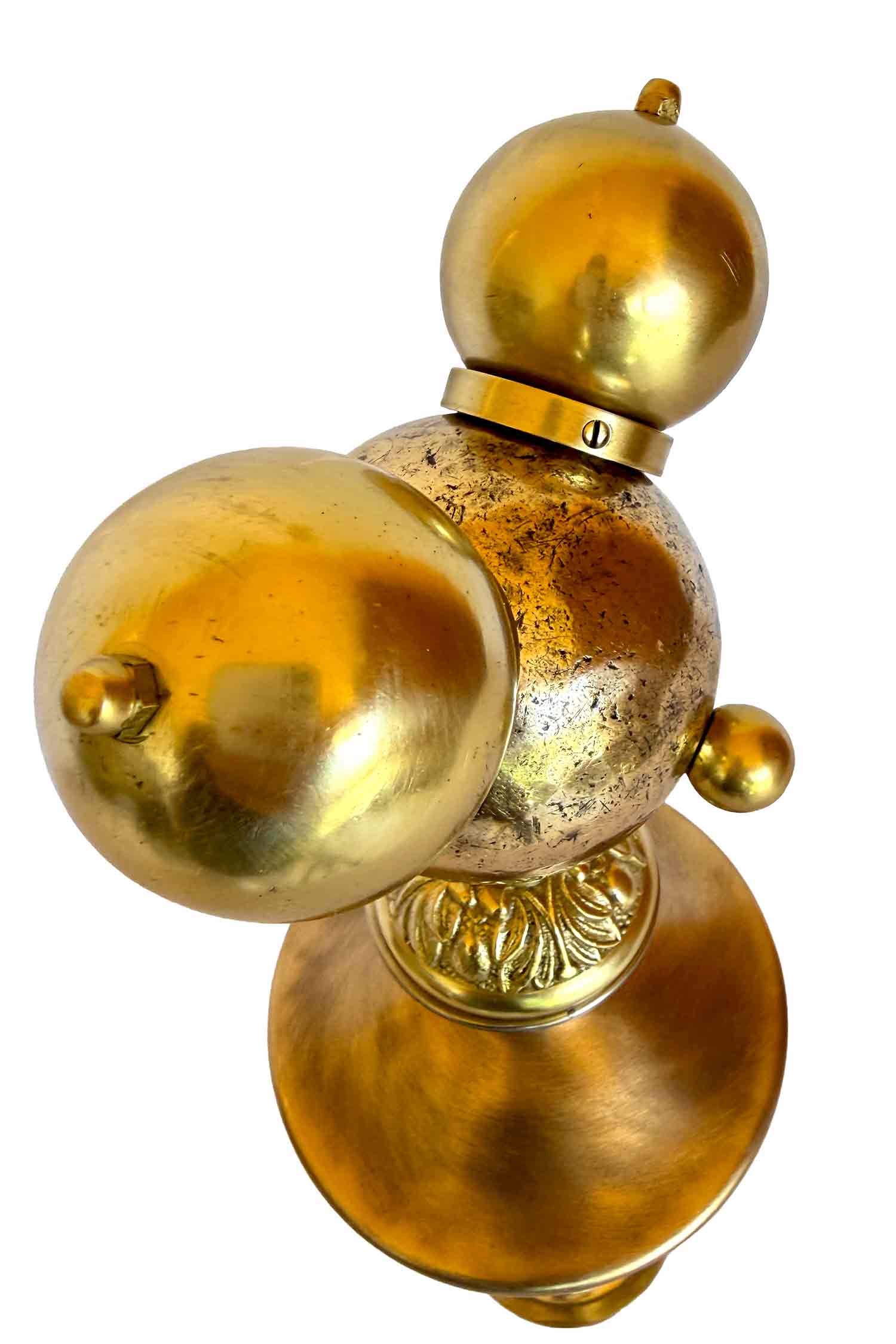 Una escultura dorada con una bola de petanca en cada cara y dos pomos a modo de orejas; el cuerpo y las piernas también están dorados y están hechos con piezas de pantallas de lámpara.