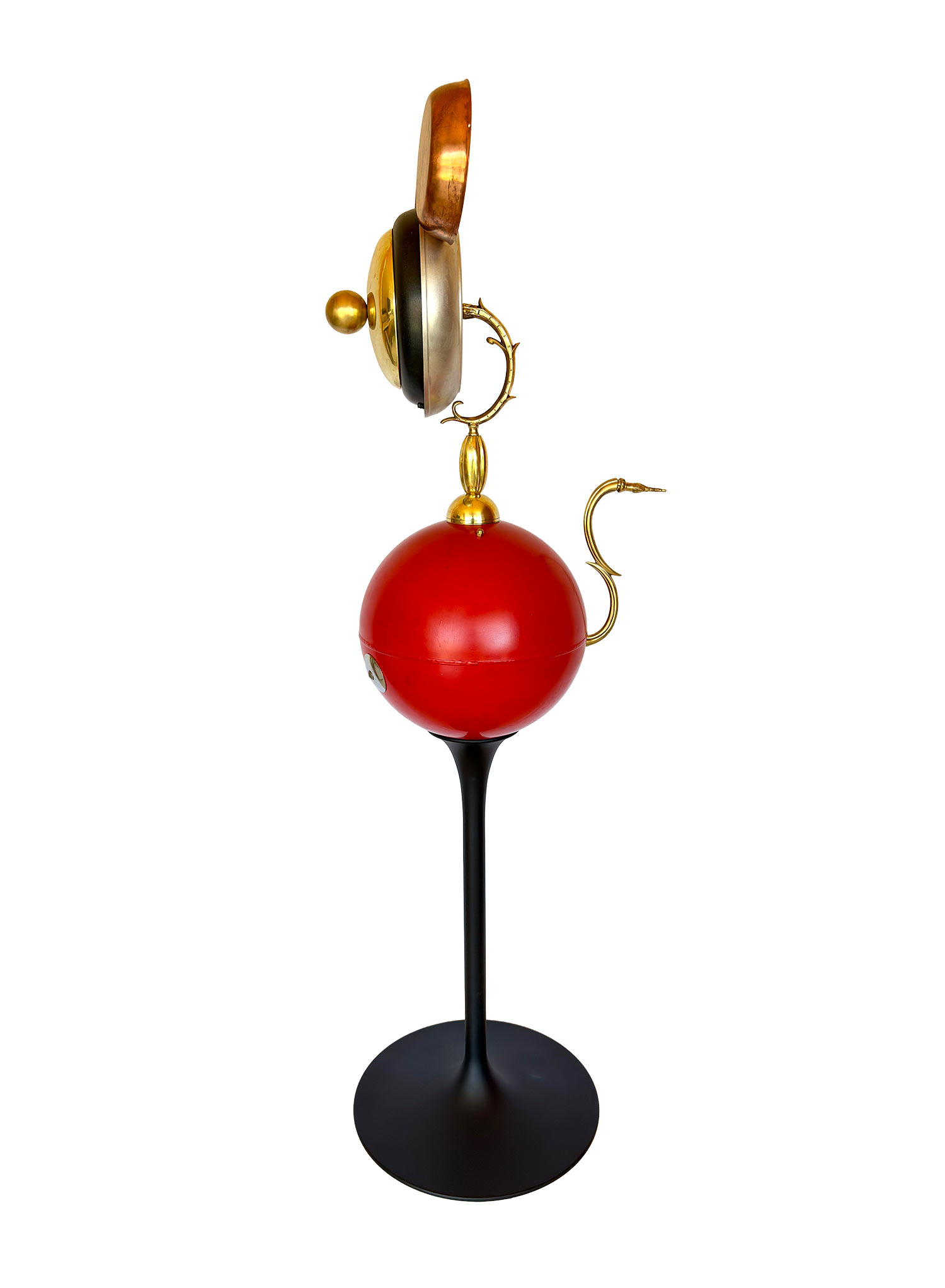 Una escultura en la que el rostro dorado está formado por una sartén y las orejas son una balanza, el cuerpo es una bola roja muy grande y las piernas son una punta tallada en negro.